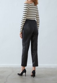 Pantalon en simili cuir noir avec une ceinture élastique, associé à un haut rayé noir et crème à épaules dénudées, porté avec des escarpins noirs.