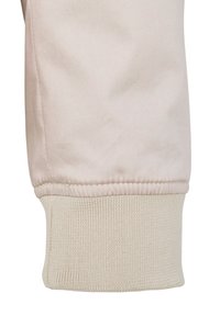 Beiger Stoffbund mit gerippter Textur, der einen sauberen Saum und ein weiches Aussehen aufweist. Das Kleidungsstück hat über dem Bund eine glatte, elegante Oberfläche.