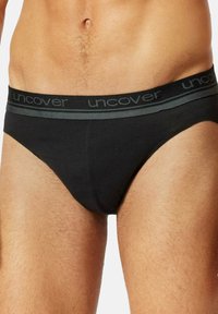 Schwarze Baumwollunterwäsche mit einem weichen, elastischen Taillenbund, der mit einem grauen Streifen und dem Wort "uncover" in schwarzer Schrift verziert ist. Glatte Textur mit leichtem Stretch.