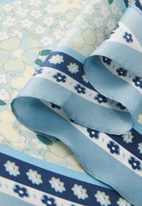 Ύφασμα με σχέδια που περιλαμβάνουν μπλε λουλούδια και ρίγες. Το υλικό φαίνεται λείο και μεταξένιο με γυαλάδα. Η χρωματική παλέτα περιλαμβάνει ανοιχτό και σκούρο μπλε.