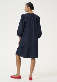 Džínové šaty s nafúknutými rukávmi, s volánovým spodkom a tmavomodrou farbou. Kombinované s jasne červenými baletkami.