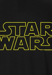 Black T-shirt featuring "STAR WARS" text in large, distressed yellow font. The design is centered, with a smooth fabric texture.