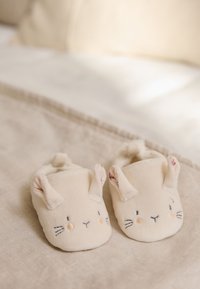 Crèmekleurige babysloffen van zachte stof met geborduurde konijnengezichten, oren en blushkleurige accenten op de wangen.