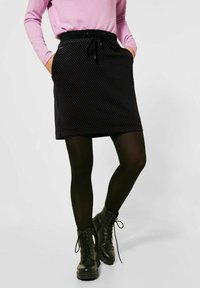 Černá sukně s potiskem a stahovacími šňůrkami v pase, v kombinaci s černými punčochami a šněrovacími vojenskými botami. Dlouhý rukáv světlého fialového topu.