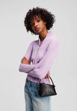 Lilac zip-up cardigan with ribbed sleeves, paired with light-wash denim. Small black handbag with logo detail. Smooth and textured materials.