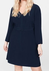 Tummansininen mekko, jossa on V-pääntie, kolmannen osan hihat ja kapea vyötärö pyöreällä vyöllä. Sileä kangas, A-linjainen siluetti.