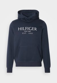 Sweat à capuche bleu marine avec poche avant et texte blanc indiquant "Hilfiger New York Est. 1985" sur la poitrine.