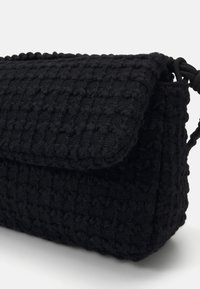 Borsa nera testurizzata con un design intrecciato, dotata di chiusura a patta e forma arrotondata. Interno liscio e dettagli hardware a contrasto.