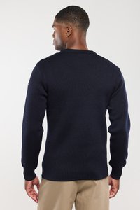 Jersey de punto azul marino con un diseño simple, puños acanalados y cuello redondo. Presenta una tela texturizada y un pequeño logotipo en el hombro.
