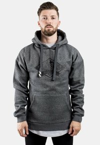 Sudadera gris con tejido texturizado, que presenta un bolsillo frontal, cordones ajustables y un logo en forma de diamante en el pecho. Manga larga y puños acanalados.