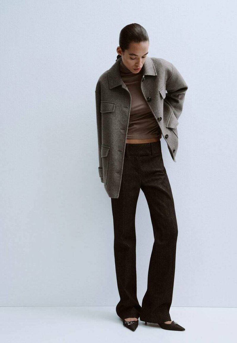 Gray wool jacket with front pockets, worn over a brown fitted top; paired with dark flared pants and pointed black shoes. Smooth textures throughout.