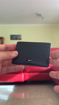 Black leather cardholder with a textured finish, featuring multiple card slots and a subtle embossed logo on the front.