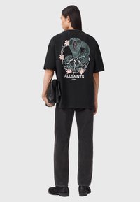 Μαύρο βαμβακερό μπλουζάκι με μεγάλο, πολύχρωμο γραφικό φίδι και λουλουδένια στοιχεία στην πλάτη, με χαλαρή εφαρμογή και κοντά μανίκια.