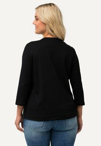 Top negro de manga larga con escote redondeado, textura suave y corte holgado. Combinado con jeans ajustados azules que tienen costuras en los bolsillos traseros.