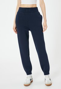 Donkerblauwe sweatpants met een hoge, gerimpelde tailleband, zijzakken en taps toelopende boorden. Gemaakt van zacht materiaal met een gladde textuur.