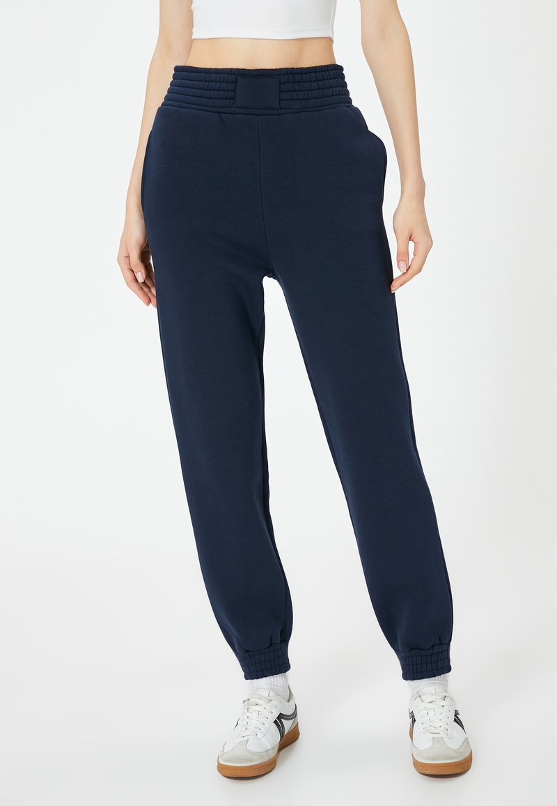 Donkerblauwe sweatpants met een hoge, gerimpelde tailleband, zijzakken en taps toelopende boorden. Gemaakt van zacht materiaal met een gladde textuur.