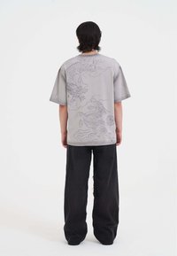 Camisa gris de manga corta con diseños de dragón y nubes, combinada con pantalones anchos negros. Textura suave, ajuste holgado y elementos gráficos detallados.
