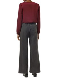 Blusa de manga larga color marrón burdeos con una textura suave, combinada con jeans de pierna ancha de talle alto en gris oscuro que cuentan con bolsillos traseros y un dobladillo deshilachado.