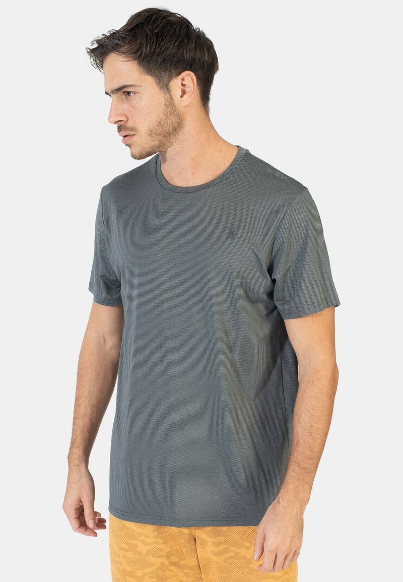 Camiseta de textura gris con mangas cortas, cuello redondo y un sutil logo en el pecho. La tela parece ligera y transpirable.