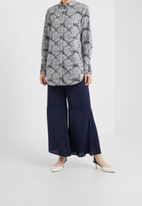 Blusa a maniche lunghe in fantasia floreale blu navy e bianca, abbinata a pantaloni larghi blu navy e scarpe con tacco bianche. Tessuto morbido e chiusura con bottoni.