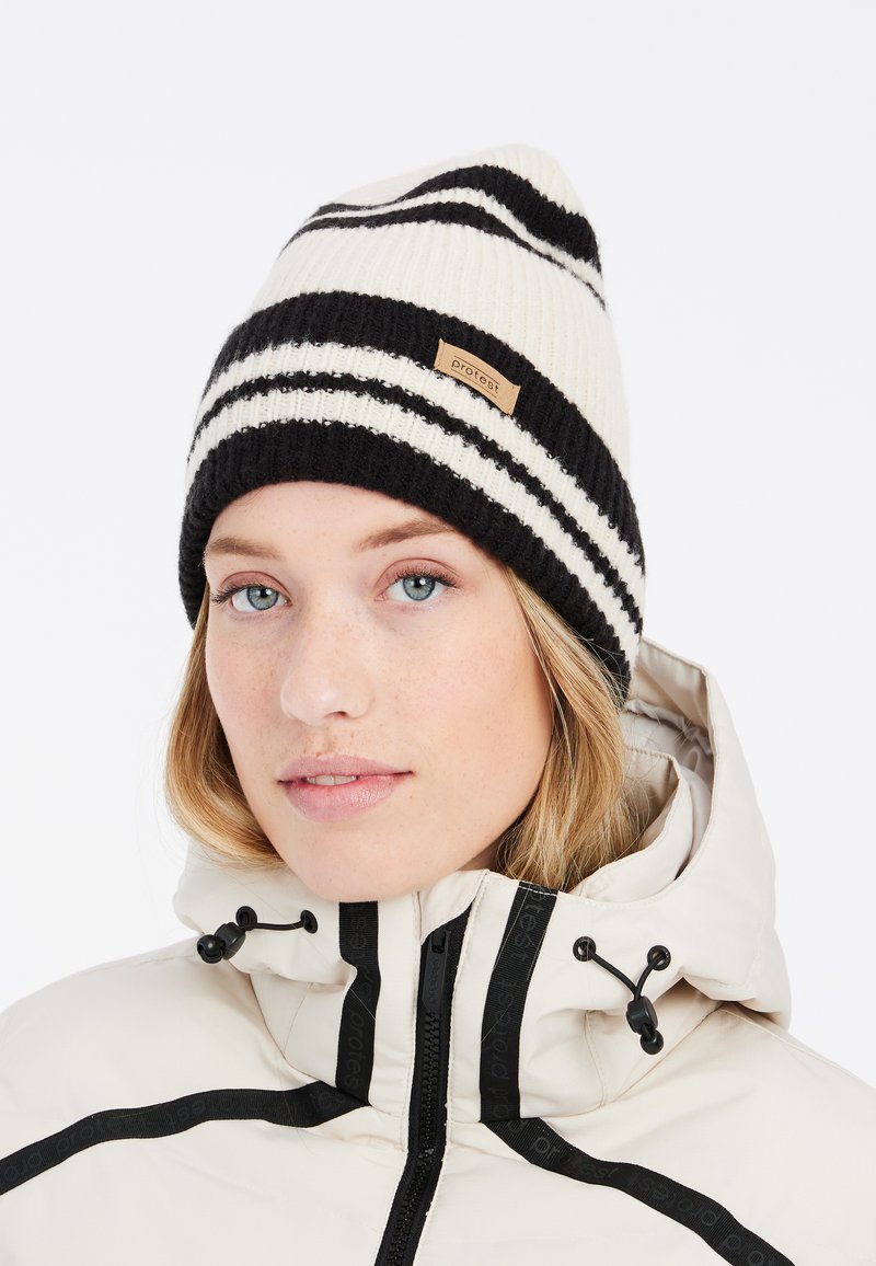 Beanie lavorato a maglia di colore bianco con strisce verticali nere, caratterizzato da una texture a coste e un piccolo etichetta logo marrone.