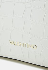 White faux leather bag featuring a crocodile texture, with a gold "Valentino" logo embossed on the front. Simple and sleek design.