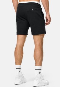 Sorte bomulds shorts med elastisk talje, to sidelommer og en baglomme med knap. Modellen har hvide sokker og sneakers på.