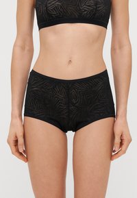 Boxers pretos de renda transparente com um padrão em onda, apresentando uma cintura elástica suave e aberturas nas pernas para um ajuste confortável.