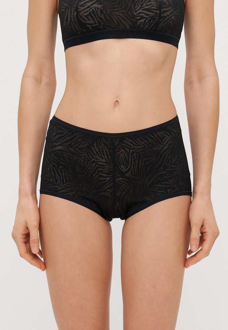 Boxers pretos de renda transparente com um padrão em onda, apresentando uma cintura elástica suave e aberturas nas pernas para um ajuste confortável.