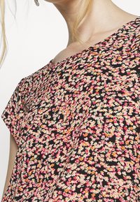Blusa floreale con sfondo nero, caratterizzata da fiori rosa, arancioni e crema. Maniche corte e vestibilità ampia con una texture di tessuto morbida.