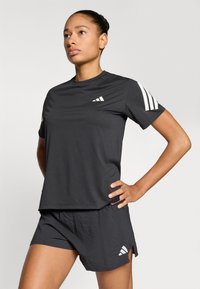 Czarny sportowy t-shirt z krótkimi rękawami, z białymi akcentami w postaci trzech pasków oraz logo, zestawiony z czarnymi spodenkami z bocznymi rozcięciami i logo.