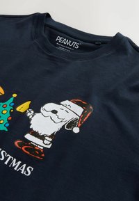 Tumed sinine puuvillane T-särk, millel on joonis karikatuurist, kes kannab jõuluvana mütsi, ümbritsetud jõululaikest ja kaunistatud kuusest, koos tekstiga "JÕULUD".