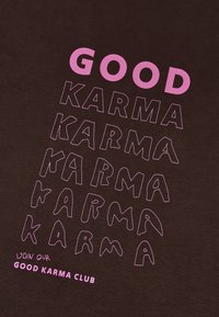 Tela marrón oscura con texto gráfico en rosa que dice "BUENA KARMA" en diferentes tamaños y estilos, con "ÚNETE A NUESTRO CLUB DE BUENA KARMA" en la parte inferior.