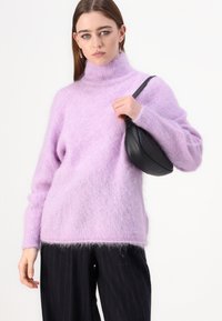 Svetlo vijoličast pulover s turtleneck ovratnikom, puhast in sproščenega kroja, dolgimi rokavi, v kombinaciji s temnimi hlačami s tankimi črtami in majhno črno torbico.
