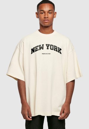 Creme oversized T-shirt med "NEW YORK" i fed sort tekst og "MERCHCODE" logo nedenunder, med korte ærmer og en afslappet pasform.