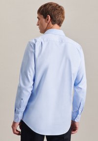 Lichtblauwe blouse met lange mouwen, een afgeronde zoom, een knoopsluiting kraag en knoopmanchetten. Gladde stoftextuur, met contrasterende hardware.