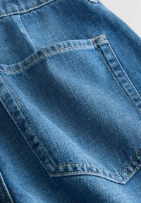 Kék farmeranyag részletes közeli képével egy dupla varrással és texturált szövési mintával ellátott hátsó zsebbel.