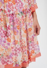 Květinové šaty z průsvitné, lehké látky. Vyznačují se vzorem květin v růžové, oranžové a fialové barvě. Texturovaný volánový detail v pase a na spodním okraji.