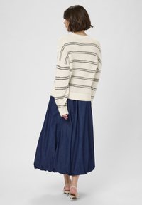 Krémszínű kötött pulóver szürke csíkokkal, egy hosszú, sötét farmer szoknyával párosítva. Puha textura, laza fit és látható varrás részletek.