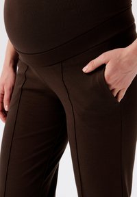 Donkerbruine zwangerschapsbroek van zacht materiaal, met een hoge taille, zijzakken en een aansluitend ontwerp met zichtbare stiksels.