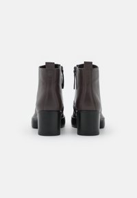 Hnědé kožené kotníkové boty s hladkým povrchem, vybavené blokovým podpatkem a zipem na zadní straně, navržené v elegantním, minimalistickém tvaru.