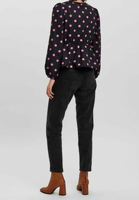 Blusa nera con pois rosa, vita peplum e maniche a sbuffo, abbinata a jeans neri e stivaletti con tacco marroni.