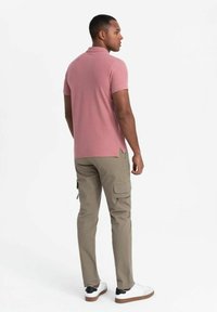 Světle růžová polo tričko s krátkým rukávem, rovný lem, v kombinaci s béžovými cargo kalhotami s několika kapsami a slim fit. Bílé boty.