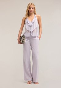 Top halter de color púrpura claro con detalles de volantes, combinado con pantalones de pierna ancha. Acompañado de un bolso de embrague con estampado de piel de serpiente y sandalias de color rosa claro.