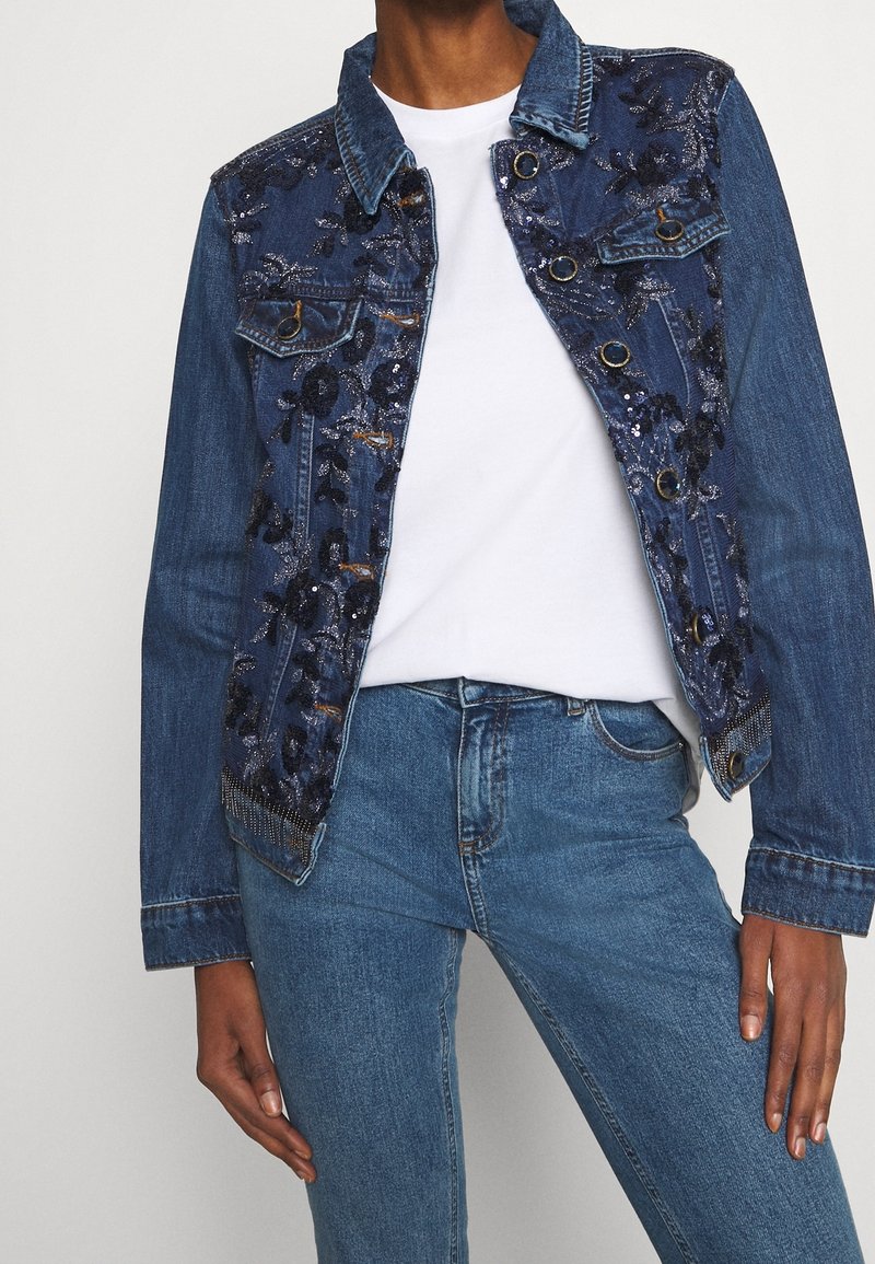 Dżinsowa kurtka w ciemnoniebieskim kolorze z haftowanym kwiatowym wzorem z cekinów na ramionach i przodzie, z zapięciem na zatrzaski oraz dwiema kieszeniami na piersi.
