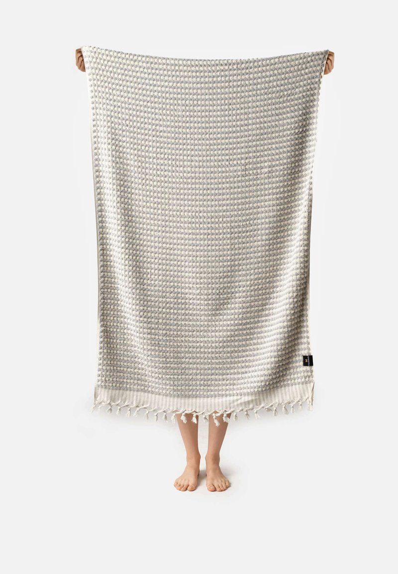 Kudottu tekstiilihuopa, jossa on vaaleanharmaa kuvio, fringed-reunat ja tekstuuri pinta. Materiaali on pehmeä ja kevyt.