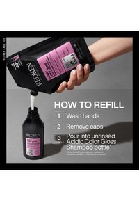 Une main verse une recharge de shampooing Redken Acidic Color Gloss dans une bouteille vide avec les instructions de recharge à côté des mains.
