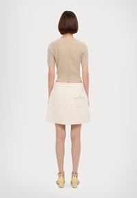 Ensemble de dos : haut en tricot beige à manches courtes, associé à une jupe A-line blanche taille haute avec une poche plaquée et un détail de bouton doré.