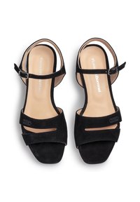 Mustat nukkaiset sandaalit, joissa on nilkkahihna, avotila ja kaksi vaakasuoraa nauhaa edessä. Vaaleankalpeat sisäpohjat, joissa on brändäys. Neliönmuotoiset korot.