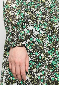Vestido floral com base preta e flores verdes e brancas, punhos franzidos com acabamento em babados e tecido leve e texturizado.
